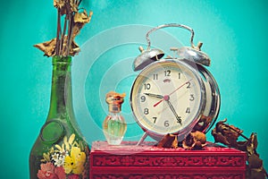 Still life with broken alarm clock, old glass vase with dead rose, perfume, vintage box