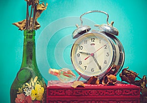 Still life with broken alarm clock, old glass vase with dead rose, perfume, vintage box