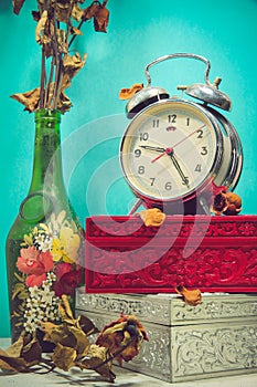 Still life with broken alarm clock, old glass vase with dead rose, vintage boxs, tone image.