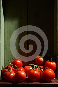 Still Life with a bunch of natural grown Tomatoes. Rustic wood background, antique wooden table