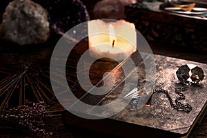 Still life with burning candle on old wooden table top, black fortune teller card, magic book and pentagram box