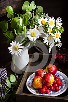 Still life with camomile flowers in jar, glass with fruit drink,peaches and cherry on the plate.