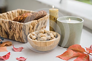 Still life candle flame, peanut, fallen leaves, wicker basket, bagel on a table, home decor in a cozy house. Autumn