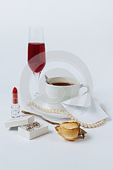 A still life with a ceramic cup of coffee, a faded rose, a coral necklace, a lipstick, a box with the silver earrings, a