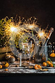 Still life with champagne bottle standing in a bucket with ice, two full flutes, sparklers and