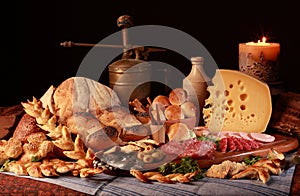 Still life with cheese, candle, italian salami, different types of bread, olives, etc.