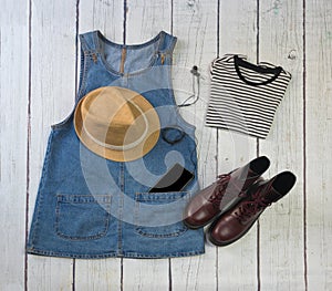 Still life of clothes, denim skirt with dungarees, striped shirt, military boots, hat, smartphone and headphones