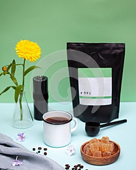 Still life of a coffee mug, a package of coffee beans, marmalade and a yellow flower in a vase on a colored background