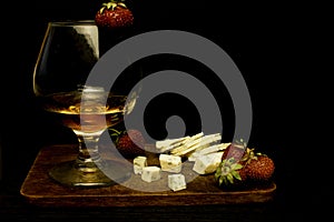Still life with Cognac and french blue cheese, strawberry on a wooden board