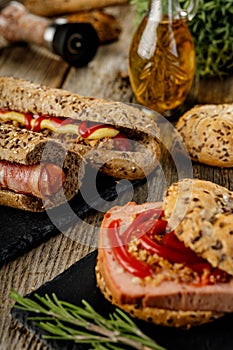 Still life composition of delicious hot dogs and sandwiches with different toppings and dried onion on the dark