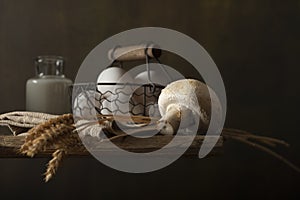 Still life composition with farm products on wooden table. Basket with eggs, bottle with milk, mushroom, wheat ears.