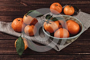 Still-life composition of fresh picked tangerines with green leaves on sack cloth and wooden background, winter time fruits and
