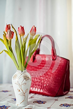 Still life composition, in home interior on the table with a tablecloth, tulips in a beautiful vase on a background of red ladies`