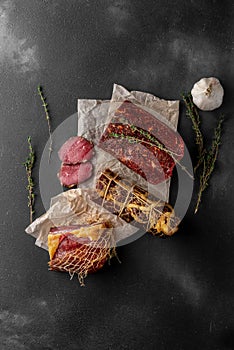 Still life composition with many pieces of red smoked dry ham on a wooden cutting board, top view