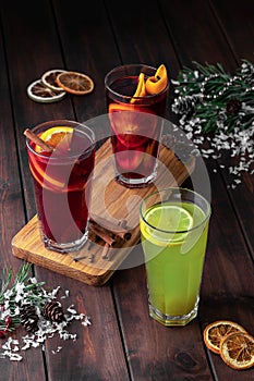 Still life composition with three glasses of red and green refreshing winter drink or mulled wine with sliced orange on a dark