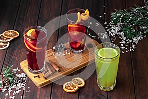Still life composition with three glasses of red and green refreshing winter drink or mulled wine with sliced orange on a dark