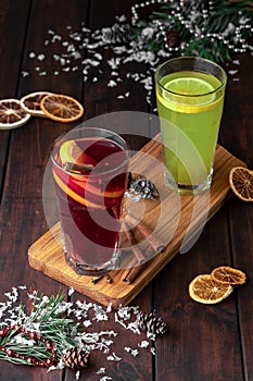 Still life composition with two glasses of red and green refreshing winter drink or mulled wine with sliced orange on a dark