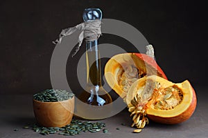 still life consisting of sunflower oil in a decorative bottle of two halves of pumpkin and lying around dried shelled