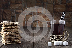 Still life with a cracker and black tea in a glass with a retro cup holder and three slices of sugar. Retro stylized photo. Close-