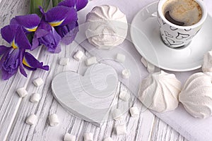 Still life with cup of coffe marshmallow zephyr iris flowers heart sign on white wooden background.