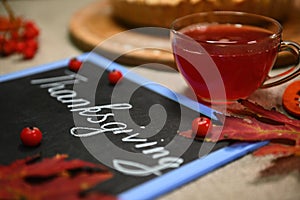 Still life. A cup with hot herbal drink and autumn maple leaves and a blackboard with lettering Thanksgiving Day.