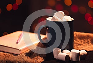 Still life. A cup with marshmallows on a background of colored lights. In the background is a colored block and a pen on it