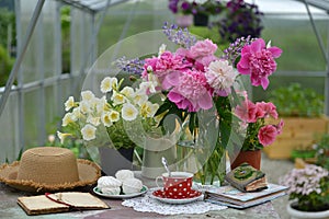 Still life with cup of tea, dessert, diary and beautiful flowers in greenhouse