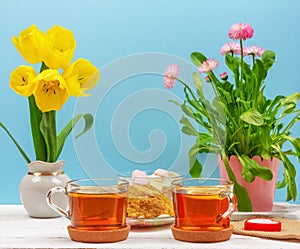 Still life with cups of tea, pieces of cake, bouquet of pink flowers in a pink pot, marshmallow and heart-shaped candle and yellow