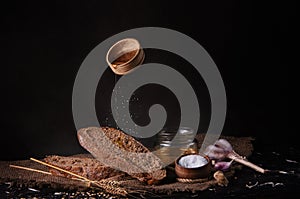 still life depicting slices of fresh bread, chestnut, honey, wheat and salt, shot in dark colors