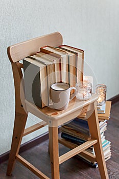 Still life details, stack of old books, cup of coffee or hot chocolate, candles on rustic bench, concept of seasonal relax time,