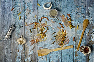 Still life of dry wheat and egg pasta with flour, a head of garlic, a salt shaker, jars with spices and wooden kitchen utensils