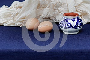 Still life with eramics pot, two eggs and textile with lace.