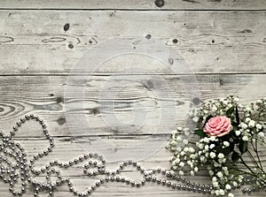 A still life flat lay concept on the light wooden background, white flowers and a pink rose accompanied with silver pearls