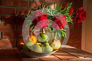 Still life with flowers and fruit against a brick wall