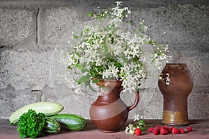 Still life with flowers in a jug, zucchini, herbs and berries on an old wooden table. Selective focus
