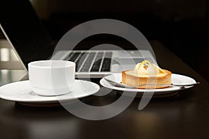 Still life with food and electronical device. A sweet delicious tartlet, cup of coffee over laptop background.