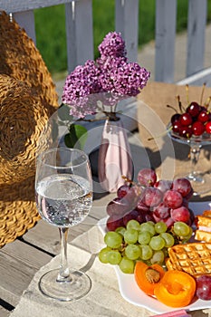Still life and food photo. A plate of fruit, a glass of water and a vase of lilacs stand on burlap on a wooden floor