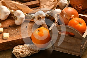 Still life of food in a rural style on a dark wood background, onion and tomatoes in a box, galic, concept of healthy food