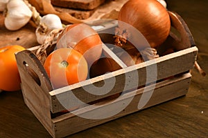 Still life of food in a rural style on a dark wood background, onion and tomatoes in a box, galic, concept of healthy food