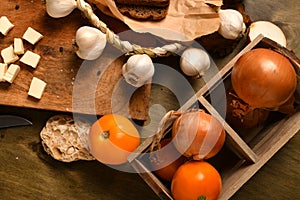 Still life of food in a rural style on a dark wood background, sliced cheese, garlic, onion and tomatoes, concept of healthy food