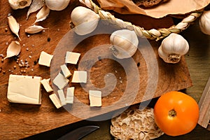 Still life of food in a rural style on a dark wood background, sliced cheese, garlic, onion and tomatoes, concept of healthy food