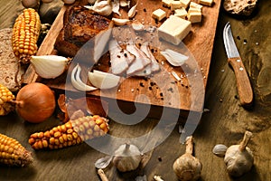 Still life of food in a rural style on a dark wood background, sliced lard and garlic, cheese, corn and onion, concept of fresh