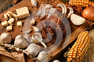 Still life of food in a rural style on a dark wood background, sliced lard and garlic, cheese, corn and onion, concept of fresh