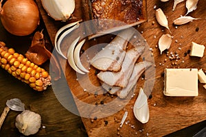 Still life of food in a rural style on a dark wood background, sliced lard and garlic, cheese, corn and onion, concept of fresh