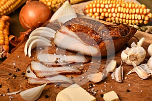 Still life of food in a rural style on a dark wood background, sliced lard and garlic, cheese, corn and onion, concept of fresh