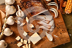 still life of food in a rural style on a dark wood background, sliced lard and garlic, cheese, corn and onion, concept of fresh