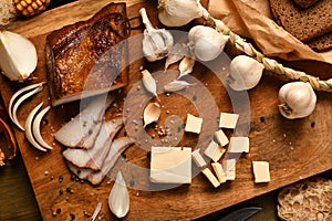 Still life of food in a rural style on a dark wood background, sliced lard and garlic, cheese, rye bread and onion, concept of