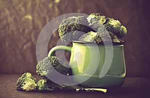 still life with fresh green broccoli in ceramic cup on black stone plate , vintage and retro color tone