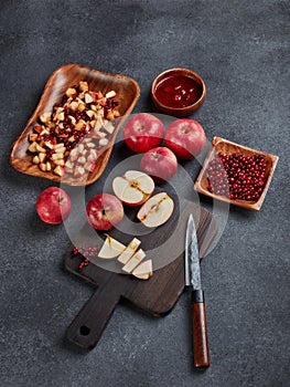 Still life with fresh lingonberries, red appples with knife on black cutting board and homemade jam on dark background. Top view