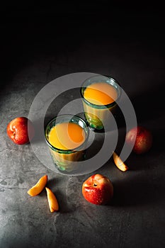 Still life of fresh nectarines with droplets of water and juice in turquoise vintage glasses on dark background. Low key